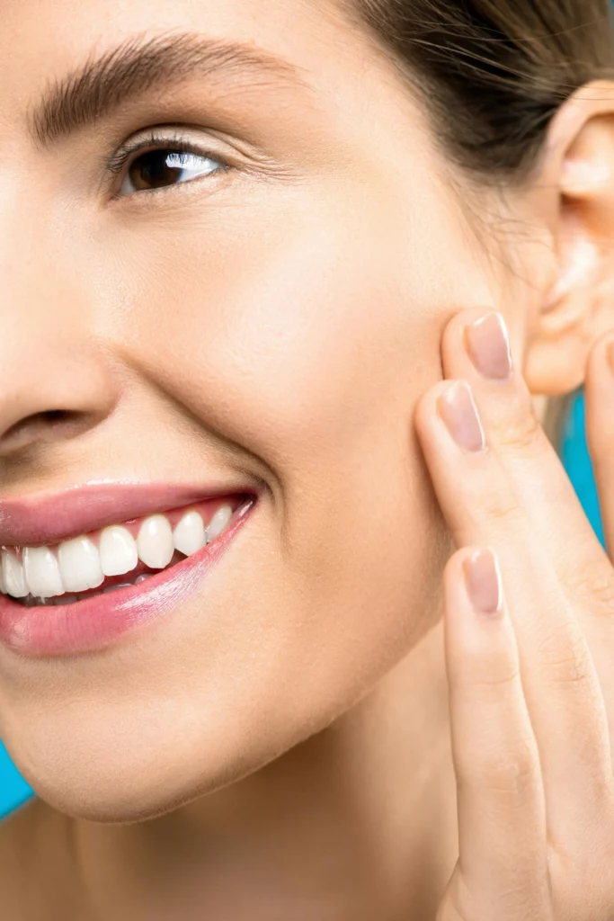 Smiling person touches smooth skin on face.