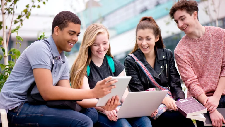 Smiling students using tablets and laptops outdoors.